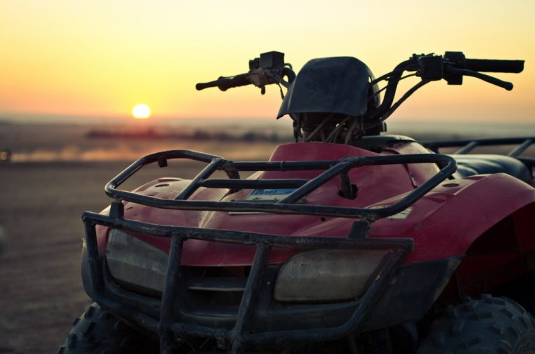 Red ATV parked on the beach with the sin setting in the background.